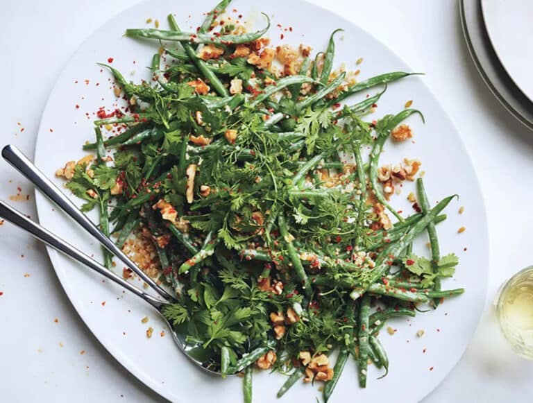 salade haricots verts, herbes avec une cuillère en métal dans un plat blanc
