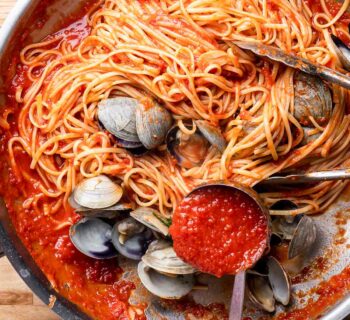 spaghetti aux palourdes et à la tomate dans une poêle avec une louche pour servir