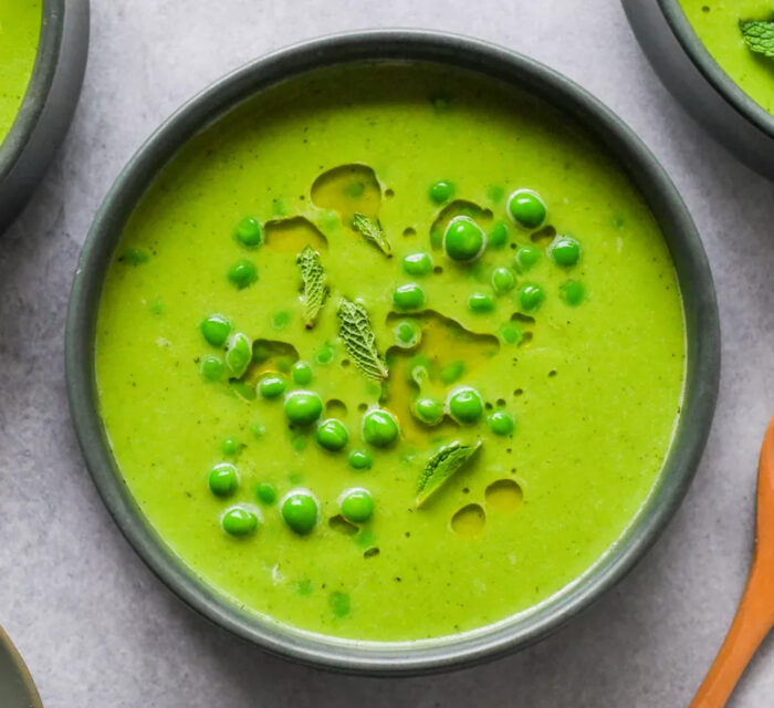 soupe de petits pois dans un bol noir avec une cuillère en bois à côté