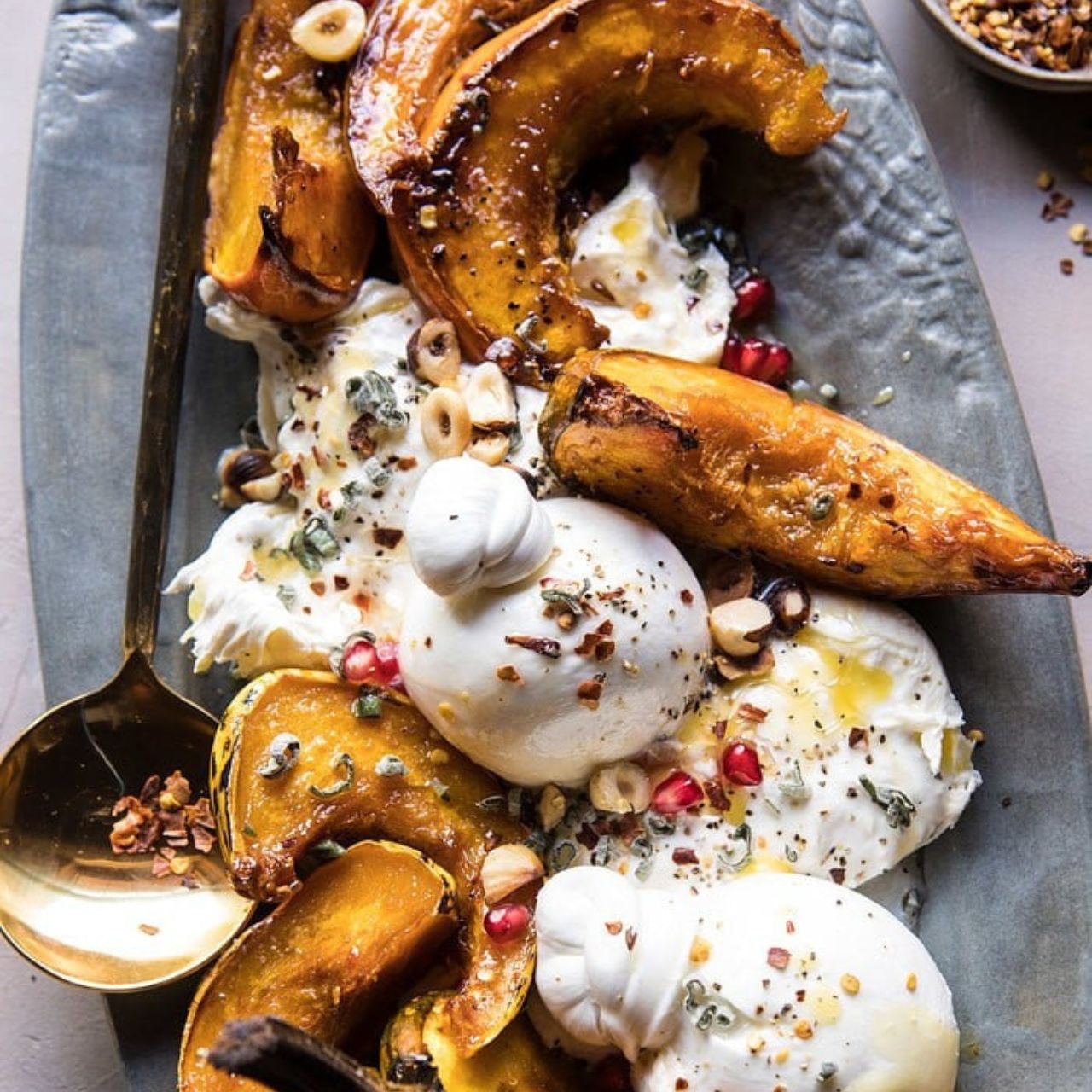 Courges et burrata cuits au four avec du buerre et du miel, servi dans un plat gris avec de la grenade