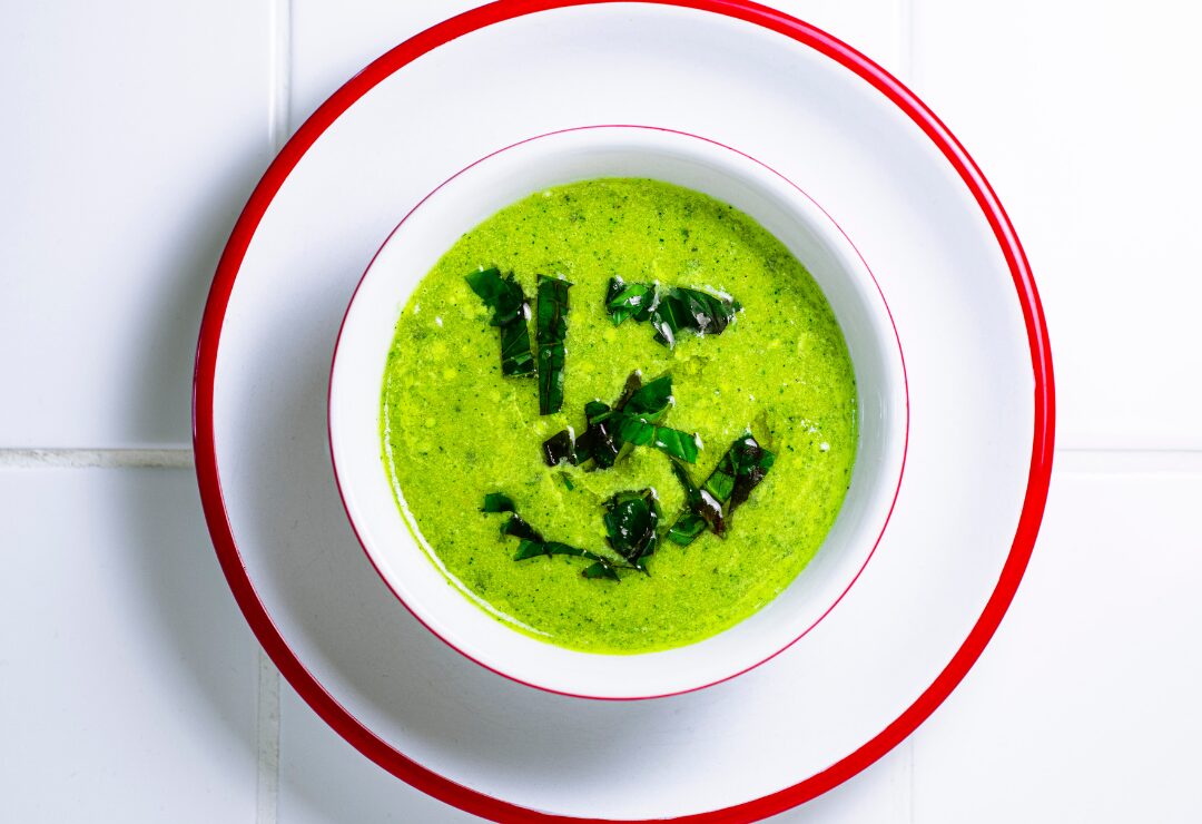 Soupe froide à la courgette avec du basilic, dans un bol blanc et assiette blanche