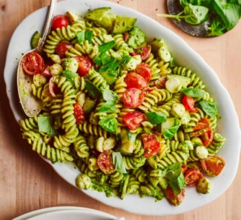 pâtes au pesto avec des tomates et de la mozzarella sur une assiette blanche avec une cuillère en acier