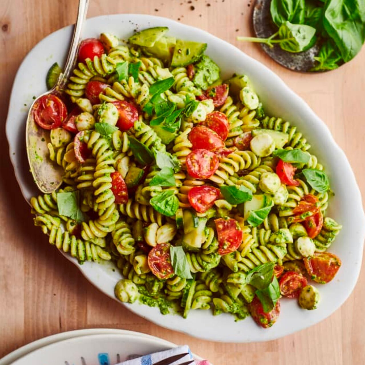 pâtes au pesto avec des tomates et de la mozzarella sur une assiette blanche avec une cuillère en acier