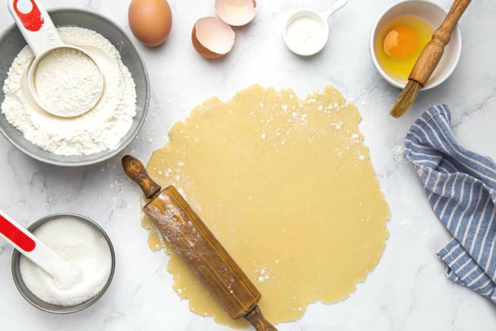 Pâte à tarte étalée avec bol de farine et jauen d'oeuf pour dorer