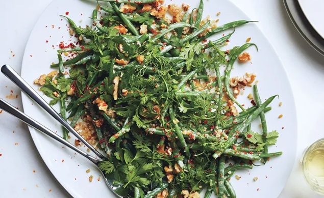 salade haricots verts, herbes avec une cuillère en métal dans un plat blanc