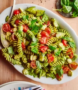 pâtes au pesto avec des tomates et de la mozzarella sur une assiette blanche avec une cuillère en acier