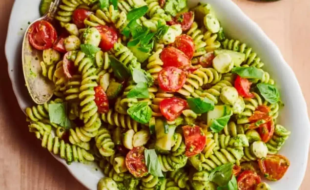 pâtes au pesto avec des tomates et de la mozzarella sur une assiette blanche avec une cuillère en acier