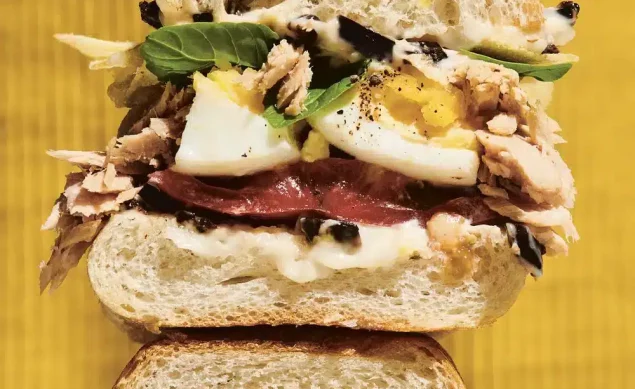 Sandwich au thon, aux œufs, salade, tomate, olives noires coupé en 2