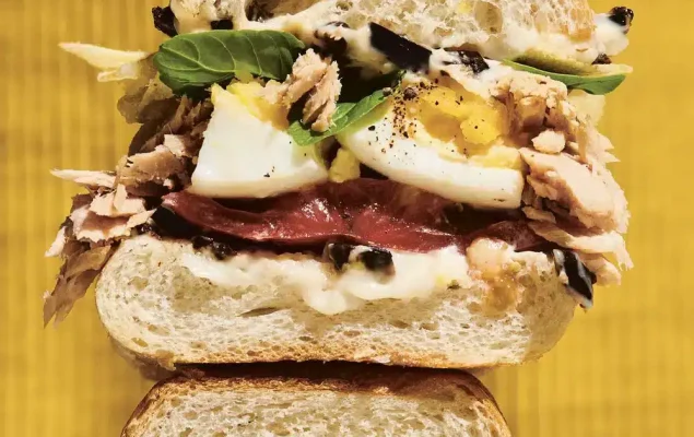 Sandwich au thon, aux œufs, salade, tomate, olives noires coupé en 2